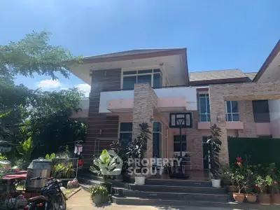 Charming two-story house with lush garden and spacious outdoor area under clear blue sky.