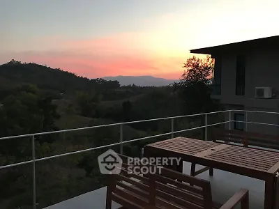 Stunning sunset view from a modern balcony with wooden furniture and scenic hills.