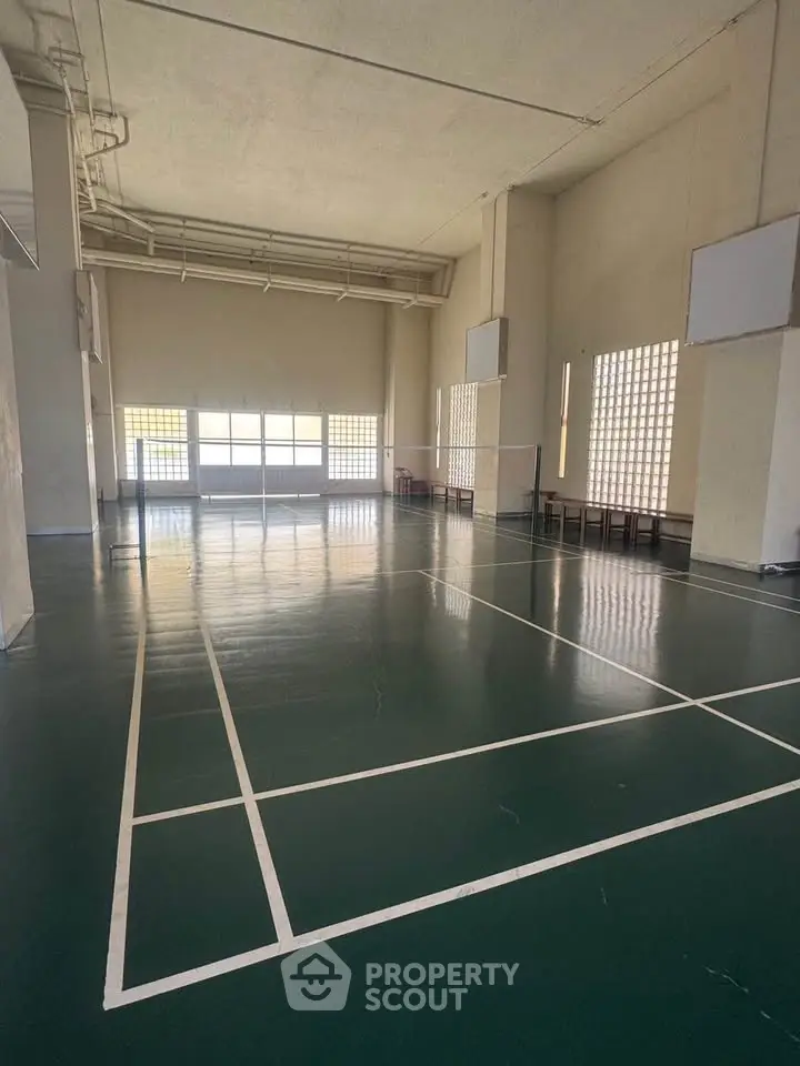Spacious indoor badminton court with high ceilings and natural light, perfect for sports enthusiasts.