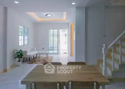 Modern open-plan living room with dining area and staircase, featuring sleek design and natural light.