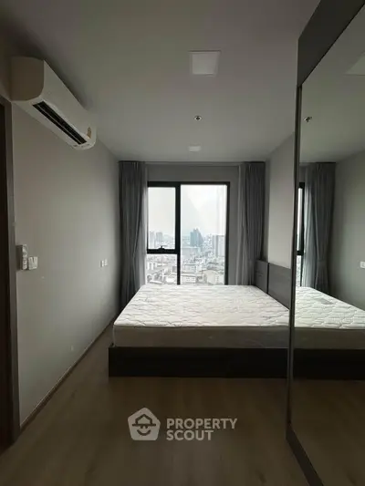 Modern bedroom with city view, featuring large window and mirrored wardrobe, perfect for urban living.