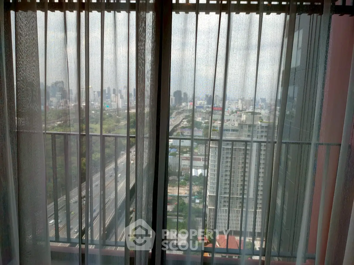 Stunning cityscape view from high-rise apartment window with sheer curtains.