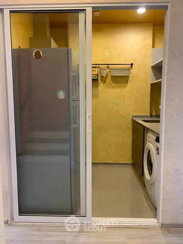 Compact kitchen with washing machine and fridge in modern apartment.