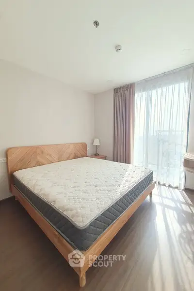 Bright and airy bedroom with wooden bed frame and large window.