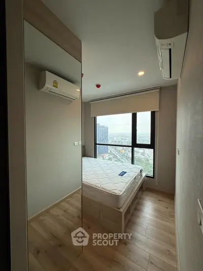 Modern bedroom with large window offering city view, featuring wooden flooring and air conditioning.