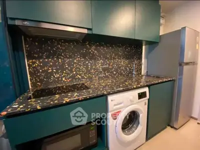 Modern kitchen with teal cabinets, terrazzo countertop, and built-in appliances including washing machine and fridge.
