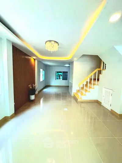 Spacious modern living room with elegant lighting and staircase, perfect for family gatherings.