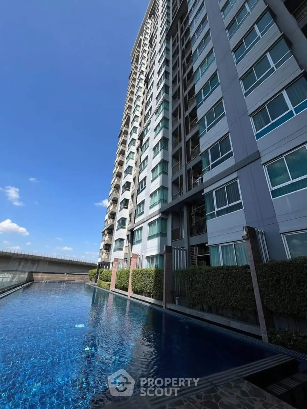 Modern high-rise building with a luxurious pool and clear blue sky.