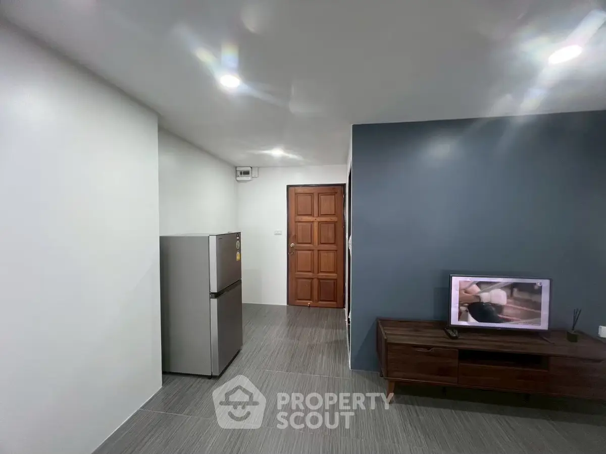 Modern living room with sleek design, featuring a wooden door, TV unit, and stainless steel refrigerator.