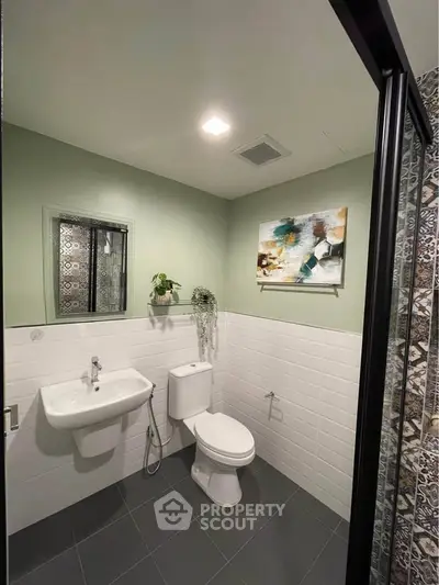 Modern bathroom with sleek design, featuring a white sink and toilet, green walls, and decorative artwork.