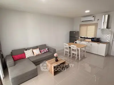 Modern open-plan living room with kitchen, featuring sleek furniture and neutral tones.