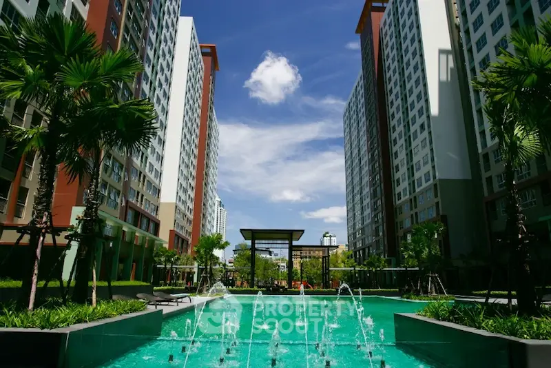 Luxurious residential complex with a stunning central pool surrounded by lush greenery and modern high-rise buildings under a clear blue sky.