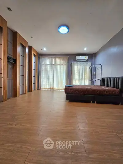 Spacious bedroom with wooden flooring and large windows for natural light.