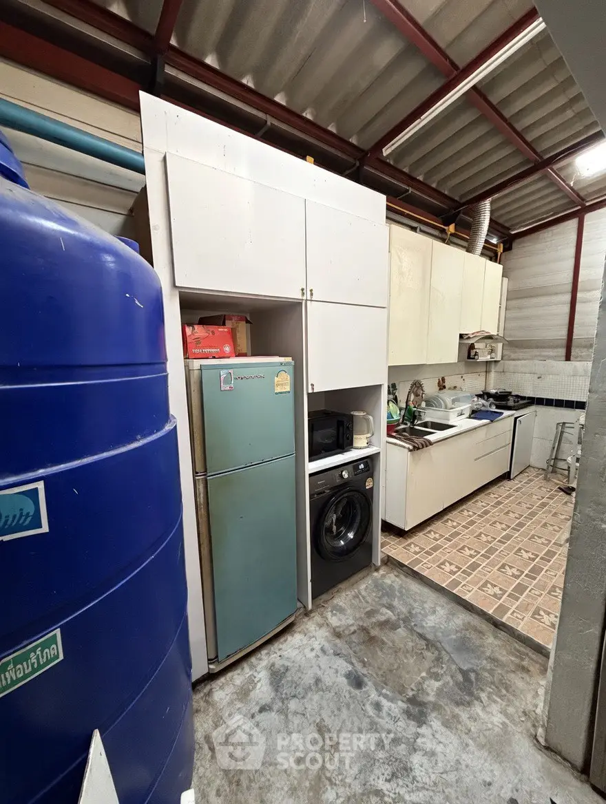 Compact kitchen with appliances including fridge and washing machine, featuring tiled flooring and storage cabinets.