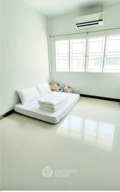 Minimalist bedroom with floor mattress and large windows for natural light.