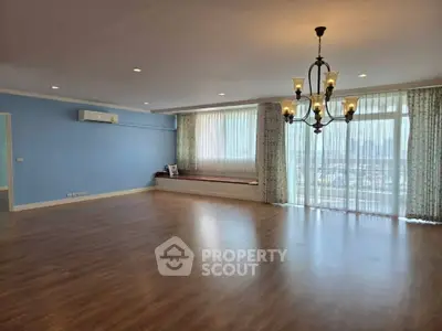 Spacious living room with elegant chandelier and large windows offering natural light.