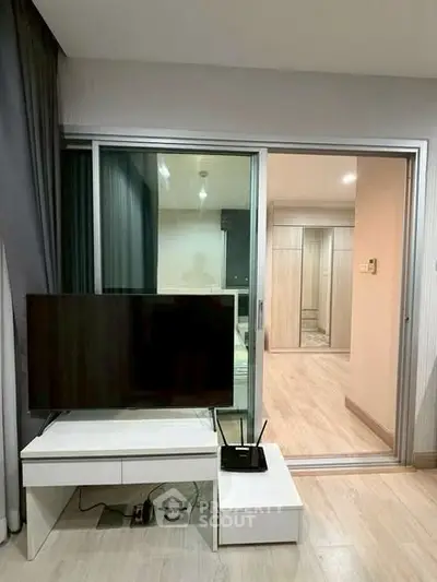 Modern living room with sleek TV setup and glass sliding doors leading to a bright hallway.