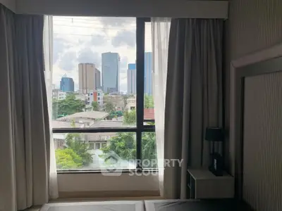 Spacious bedroom with large window offering stunning city skyline view, perfect for urban living.
