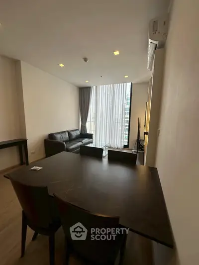 Modern living room with sleek furniture and large window offering city views.