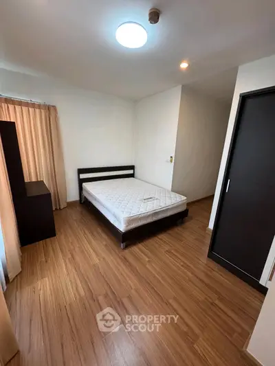 Spacious bedroom with wooden flooring and natural light