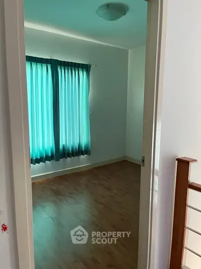 Spacious empty room with wooden flooring and large window with blue curtains.