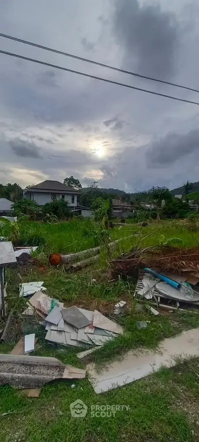 Scenic view of a residential plot with lush greenery and a distant house under a cloudy sky.