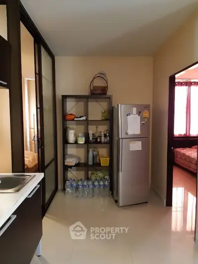 Modern kitchen with stainless steel fridge and open shelving, adjacent to a cozy bedroom.