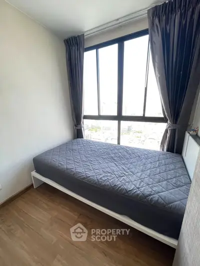 Cozy bedroom with large window and city view, featuring a comfortable bed and elegant curtains.