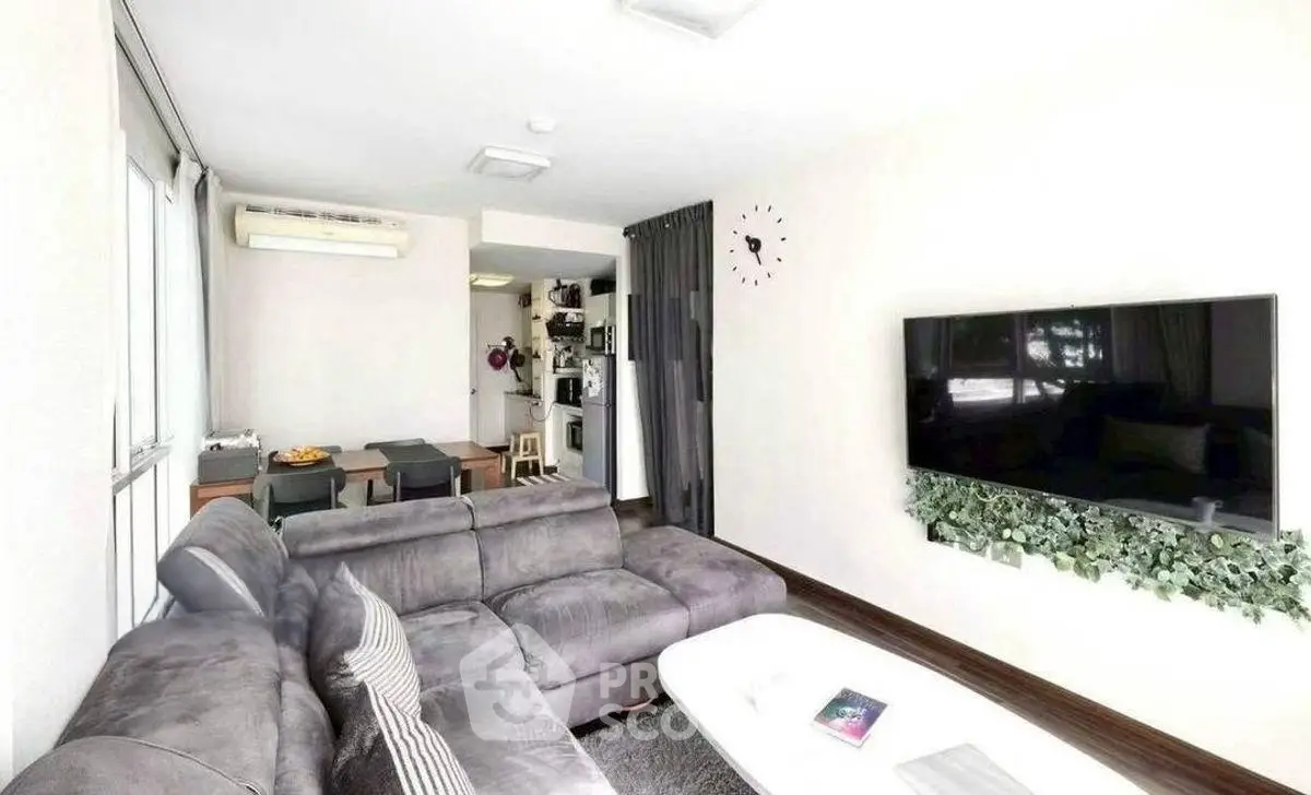 Modern living room with plush sofa and wall-mounted TV, open to dining area and kitchen.