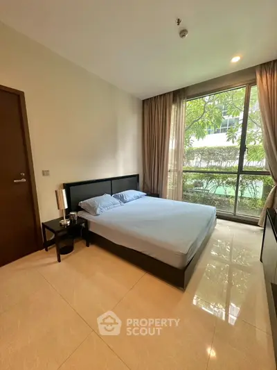 Spacious bedroom with large window and modern furnishings in a luxury apartment.