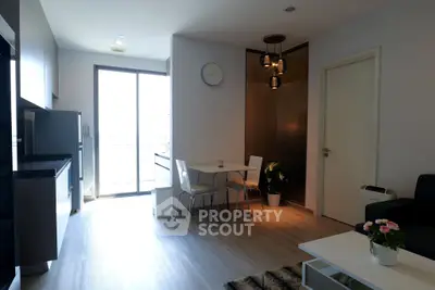 Modern living room with open kitchen, stylish decor, and natural light from large window.