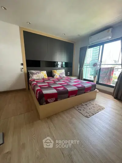 Modern bedroom with large window and city view, featuring stylish decor and wooden flooring.