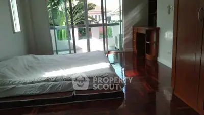 Spacious bedroom with polished wooden floors and large windows opening to a balcony.