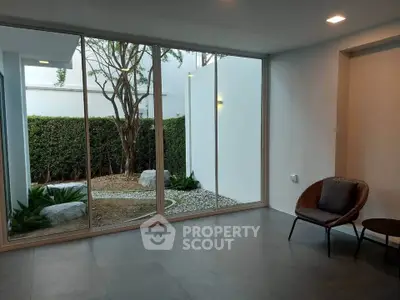 Modern interior with large windows overlooking a serene garden, featuring sleek flooring and minimalist furniture.