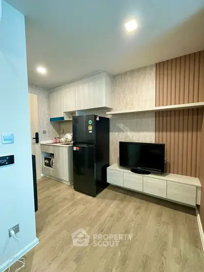 Modern apartment interior with sleek kitchen and cozy living area featuring TV and fridge.
