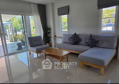 Modern living room with stylish gray furniture and large windows offering natural light and garden view.