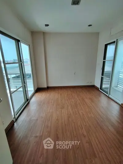 Spacious empty room with wooden flooring and large windows.