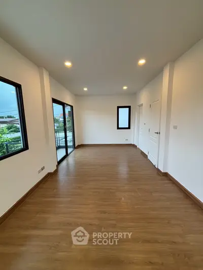 Spacious unfurnished room with wooden flooring and large windows offering natural light.
