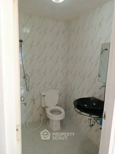 Compact bathroom with modern fixtures and tiled walls, featuring a toilet, sink, and shower area.