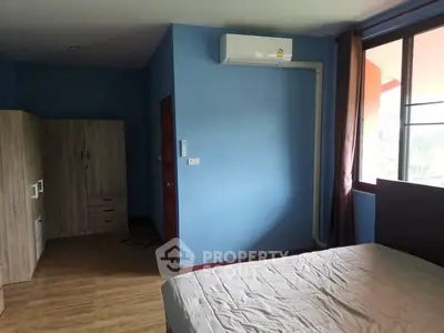 Spacious bedroom with blue walls, large window, and air conditioning unit.