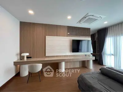 Modern living room with sleek wooden paneling and large TV, featuring stylish furniture and natural light.