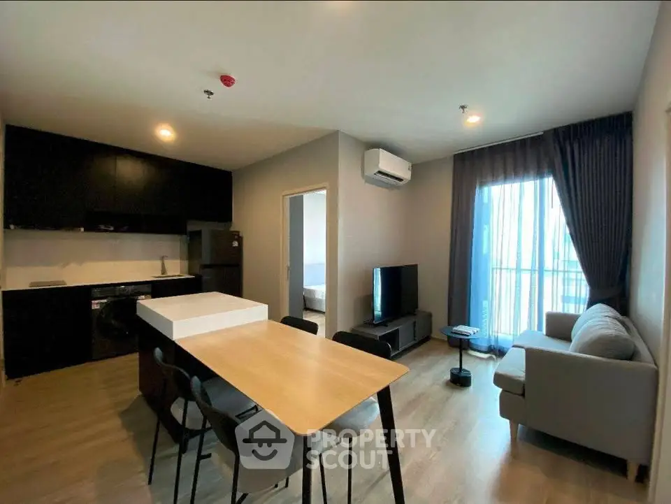 Modern open-layout living room with kitchen, featuring sleek furniture and natural light.