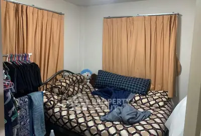 Cozy bedroom with patterned bedding and ample natural light from curtained windows.