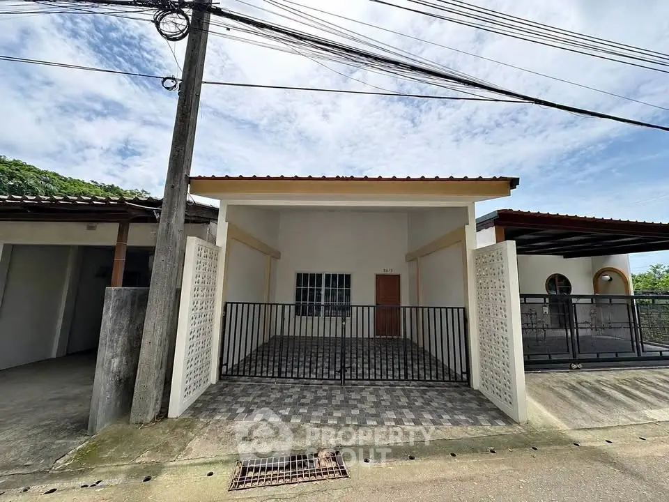 Charming single-story home with gated entrance and tiled driveway under a clear blue sky.