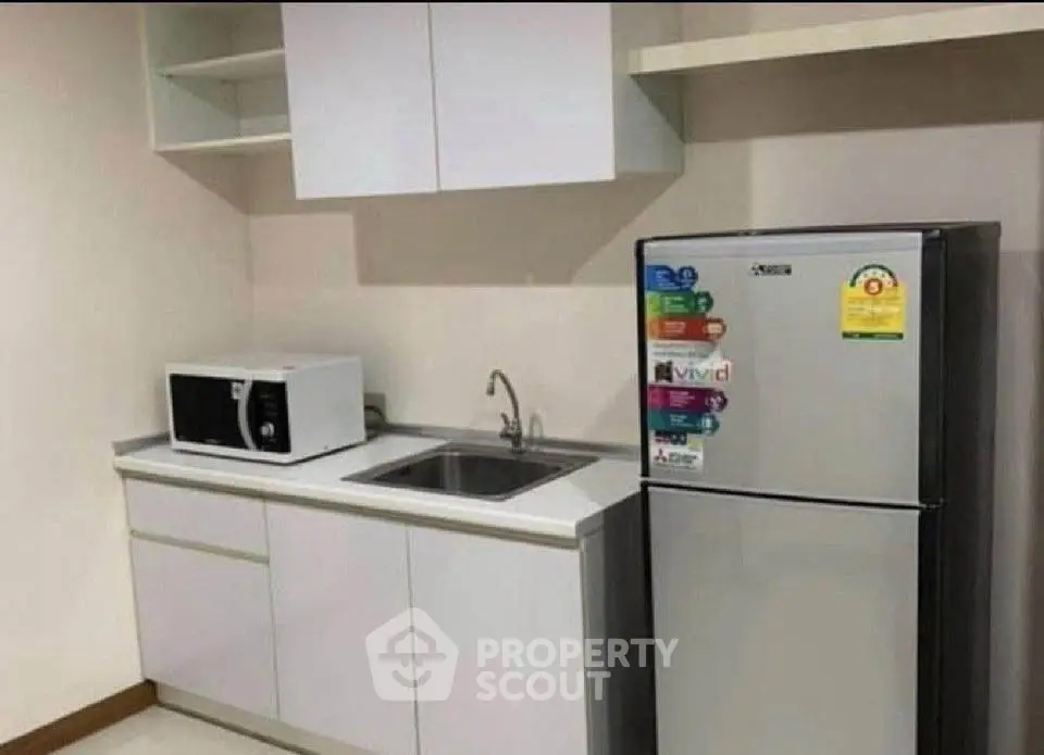 Modern kitchen with sleek white cabinets, microwave, and stainless steel fridge.