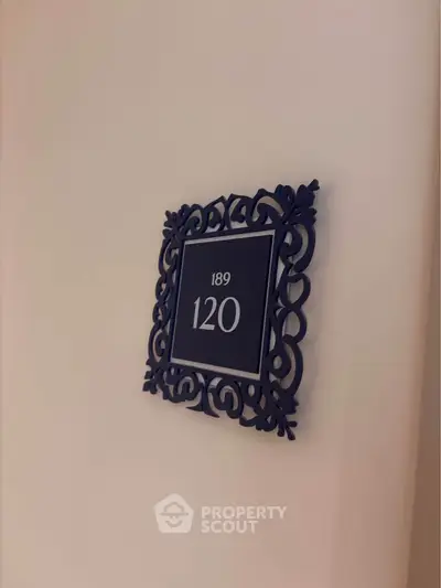 Elegant room number plaque with intricate frame design on a wall.