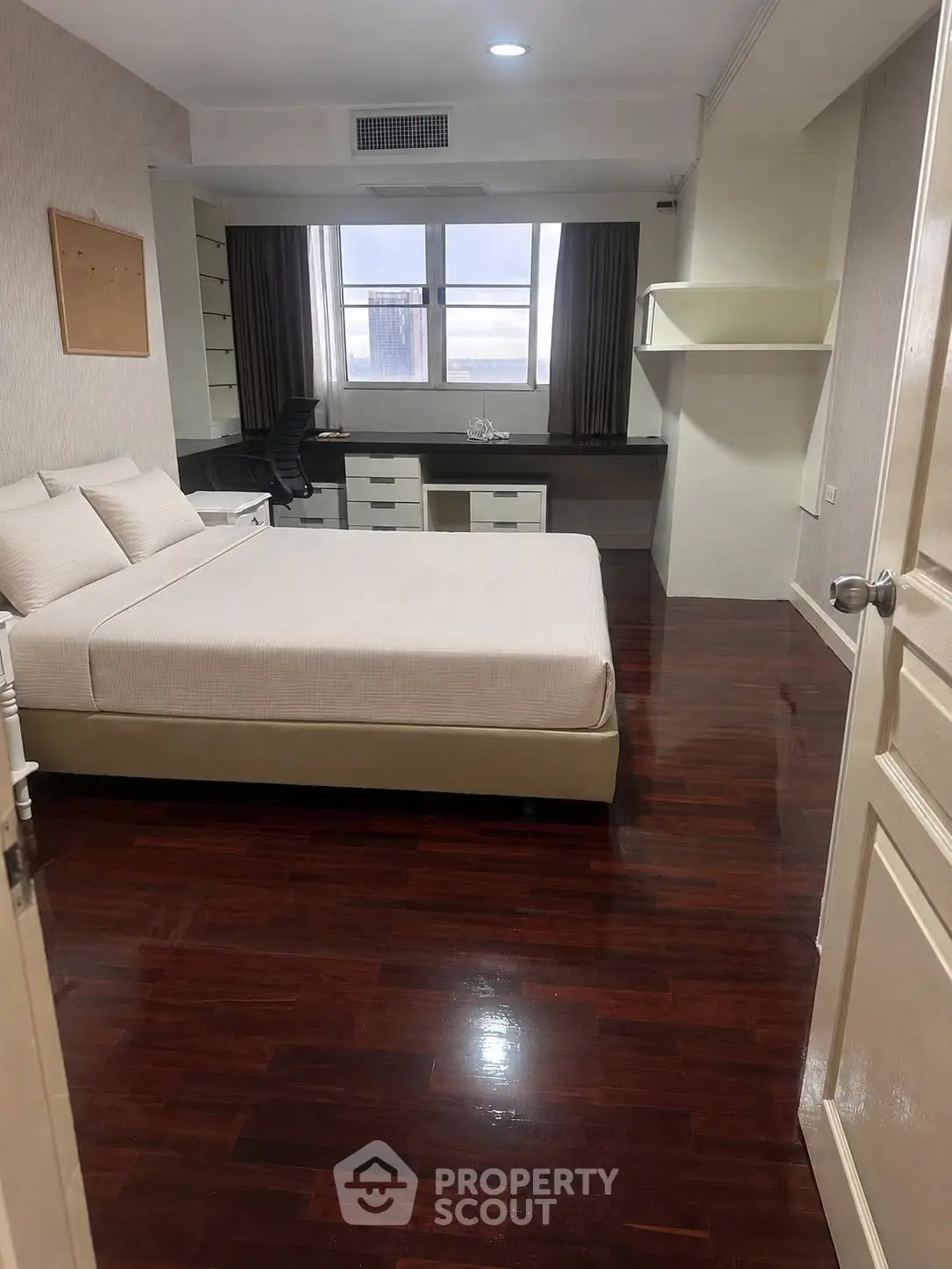 Spacious bedroom with polished wooden floors and modern furnishings in a well-lit apartment.