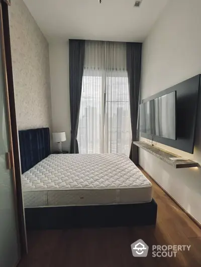 Elegant bedroom with a large window allowing natural light, complemented by dark curtains, a plush bed, and a sleek wall-mounted TV.