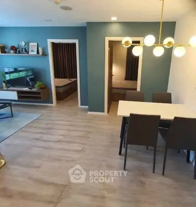 Modern open-plan living and dining area with stylish lighting and two visible bedrooms.