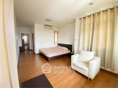 Spacious bedroom with wooden flooring and cozy seating area in modern apartment.